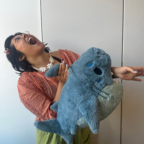 Image shows a woman holding the stuffed shark, pretending to bite her arm. It is about the size of her torso.
