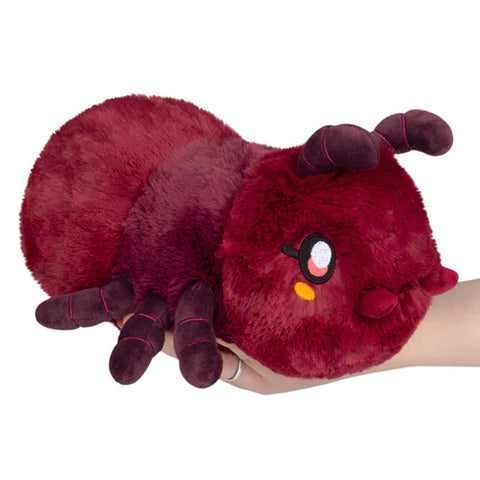 Plush toy resembling a red ant held in a hand on a white background