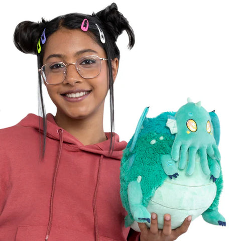 A young woman holds the plush Cthulhu in her hands. It is slightly larger than her head.