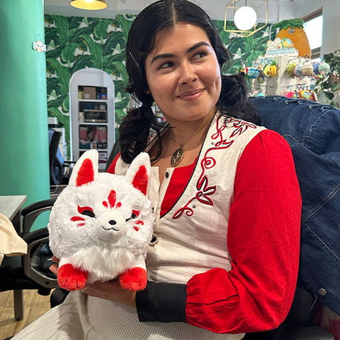 A woman holds the plush kitsune. It is slightly larger than her head.