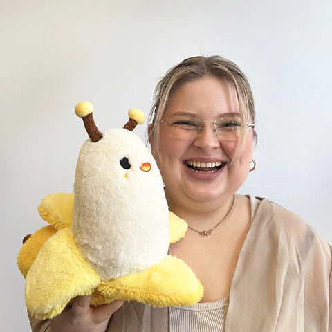 Image shows a woman holding the stuffed banana slug up to her face. It is slightly larger than her head.