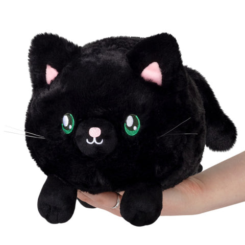A plush toy resembling a black kitty with pink inner ears and green eyes, being held in a person's hand.