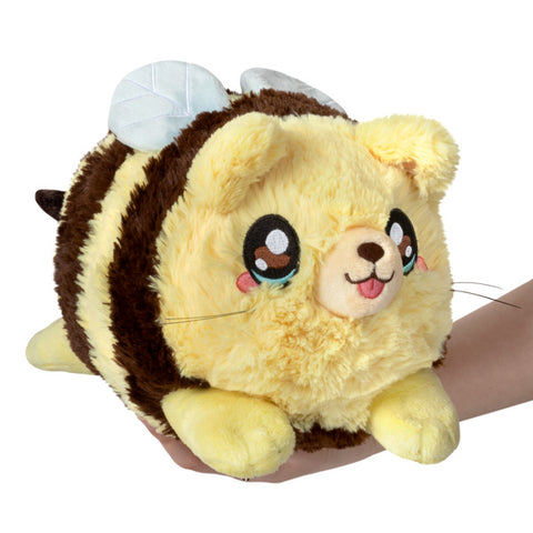 A plush toy resembling a chubby, cartoon-style bee with a cat face, with a yellow and brown color scheme, made of soft material, being held in a person's hand.