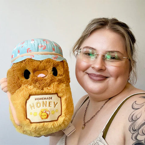 A woman holds the plush honey jar near her face. It is slightly larger than her head.