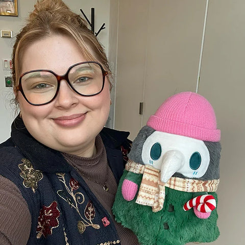 Image shows a woman holding the stuffed cozy plague doctor. It is slightly larger than her head.