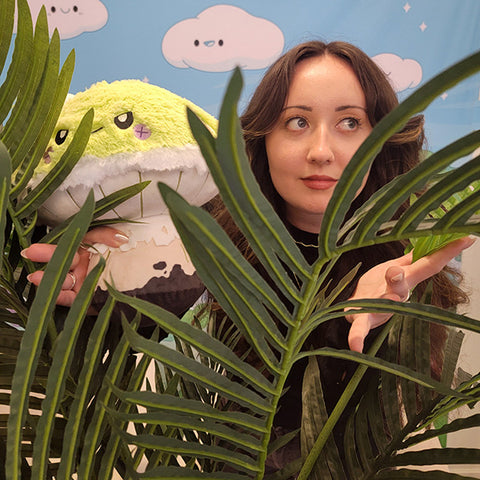 Image shows a woman hiding behind ferns holding the deathcap mushroom. It is slightly larger than her head.