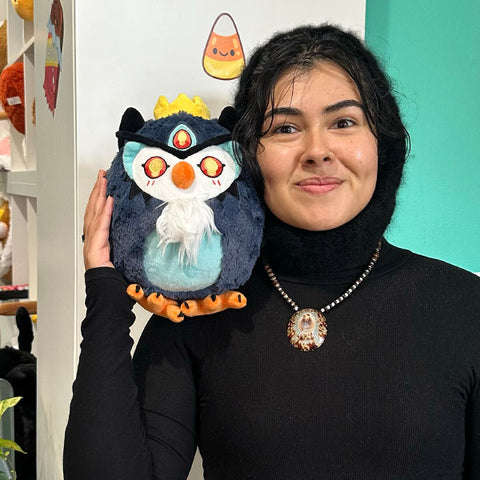 A woman holds the plush demon owl near her face. It is slightly larger than her head.
