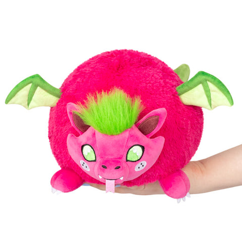 A bright pink and green plush dragon with a round body, held in someone's hand
