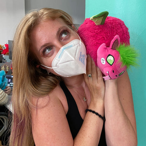 A woman holds the plush dragon up to her face. It is slightly larger than her head.