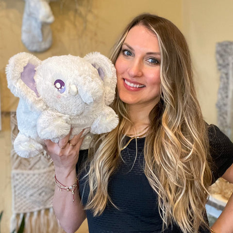 Image shows a woman holding the stuffed elephant up to her face. It is slightly larger than her head.