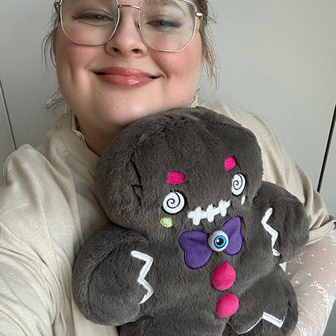 Image shows a woman holding the stuffed evil gingerbread man. It is slightly larger than her head.