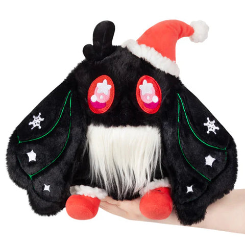 Image shows a stuffed black baby mothman with a white beard, red shoes, a red santa hat, and white snowflakes in his wings.