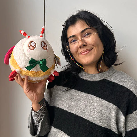 Image shows a woman holding the stuffed festive moth up to her head. It is slightly larger than her head.