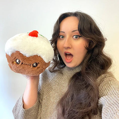 A woman holding the plush fruitcake toy. It is slightly larger than her head.