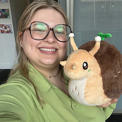 Image shows a woman holding the stuffed snail to her shoulder. It is slightly larger than her head.