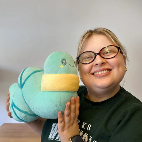 A woman holding the plush glow worm. It is slightly larger than her head.
