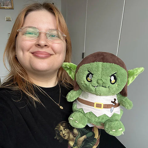 A woman holds the plush goblin near her face. It is slightly larger than her head.