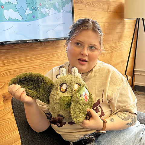 Image shows a woman holding the stuffed goblincore baby mothman. His body is about the size of her head.