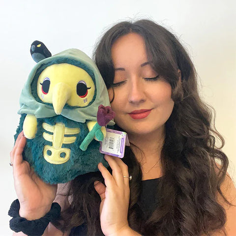 A woman holding the plush graveyard-themed plague nurse. It is slightly larger than her head.