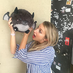 A woman holds the plush bat near her head. It is slightly larger than her head.