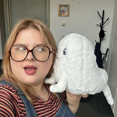 Image shows a woman holding the stuffed seal up to her ear. It is slightly larger than her head.