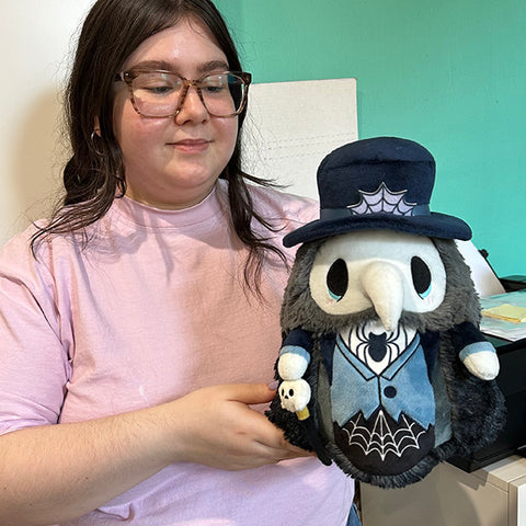 A woman holds the plush haunted plague doctor. It is slightly larger than her head.