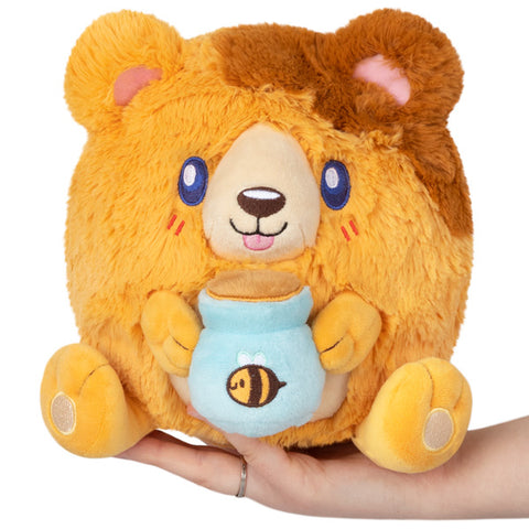 A plush bear with a round body and holding a pot of honey, held in someone's hand.