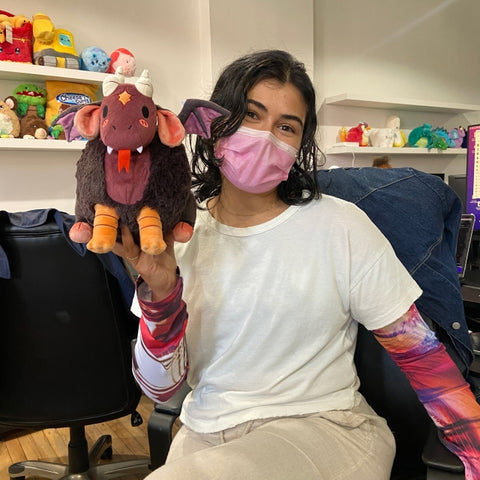 A woman holds the plush jersey devil near her face. It is slightly larger than her head.