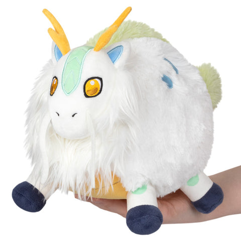 A plush toy resembling a mythical Kirin with white body, yellow horns, blue and green details, held in someone's hand.
