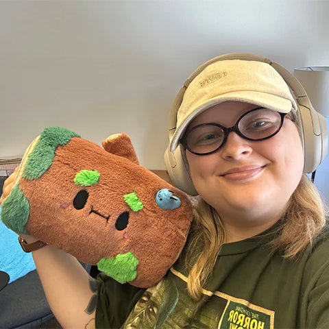 A woman holds the stuffed log. It is slightly larger than her face.