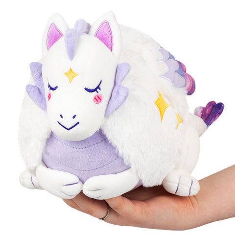 A plush toy resembling a mini lunar dragon with white body, purple accents, and gold stars, being held in a person's hand.