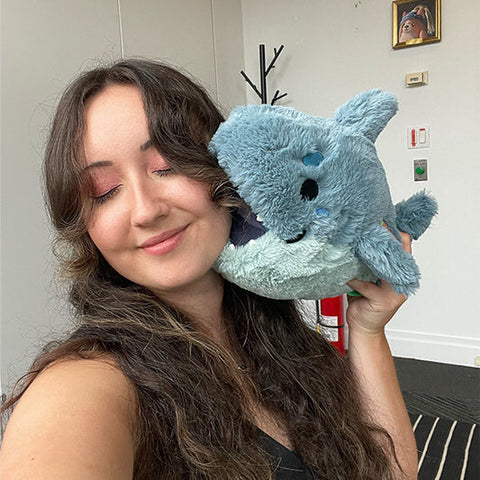 Image shows a woman holding the stuffed megalodon up to her face. It is slightly larger than her head.
