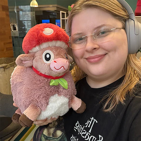 Image shows a woman holding up the stuffed mushroom cow. It is slightly larger than her head.