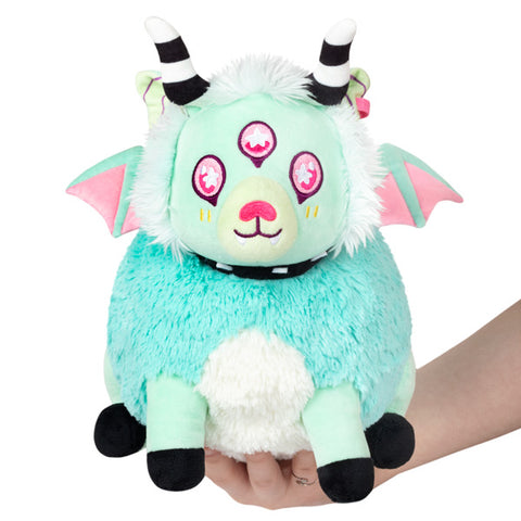 A plush toy resembling a pastel-colored creature with horns, three eyes, and wings, held in someone's hand.