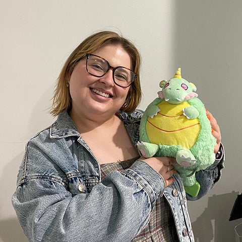 A woman holds the plush petal dragon near her face. it is slightly larger than her head.