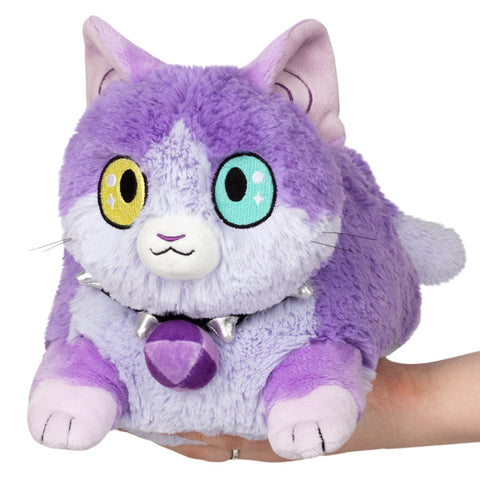 A plush toy resembling a purple cat with large eyes - one yellow and one green - held in someone's hand.