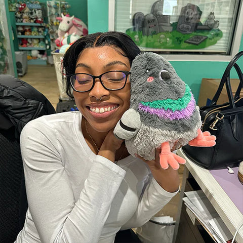 A woman holds the plush pigeon to her face. It is slightly larger than her head.
