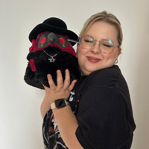 A woman holds the plush demon plague doctor up to her face. It is slightly larger than her head.
