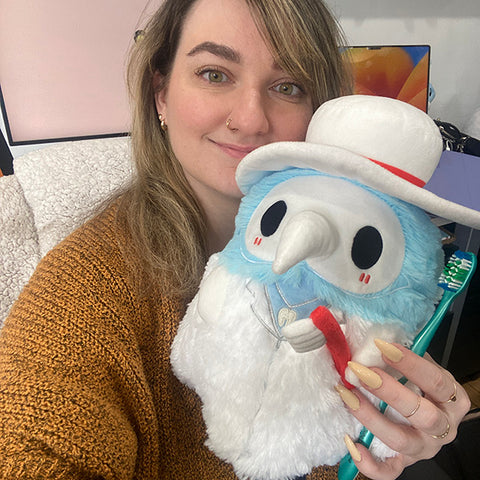 A woman holds the plush dentist Plague Doctor near her face. It is slightly larger than her head.