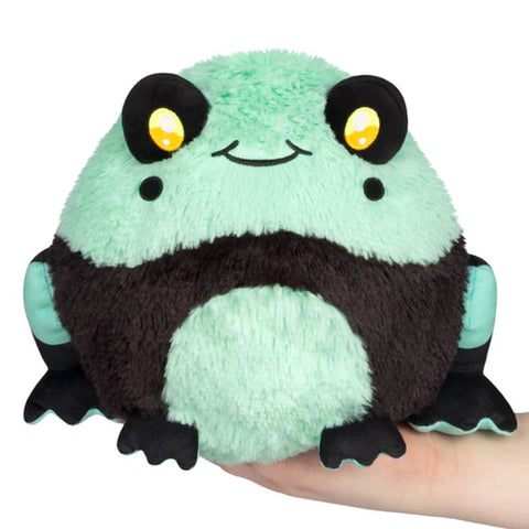 Plush toy frog with bright teal body and black legs held in a hand on a white background