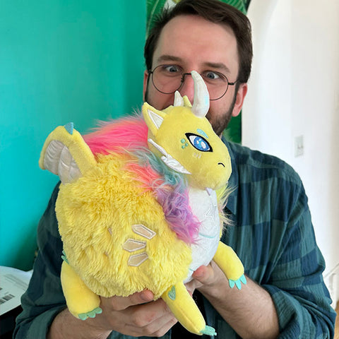 Image shows a man holding the stuffed dragon. It is slightly larger than his head.