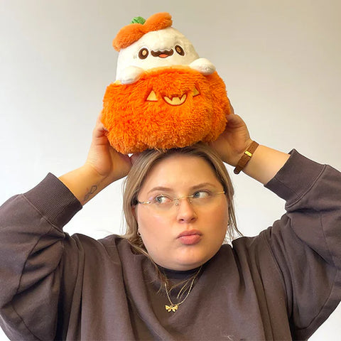 Image shows a woman holding the stuffed pumpkin ghost above her head. It is slightly larger than her head.