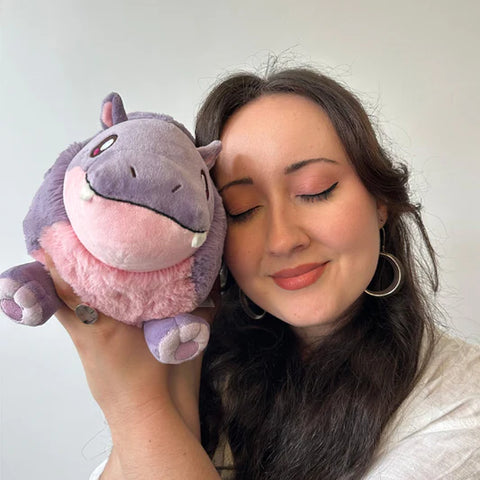 A woman holds the plush pygmy hippo near her face. It is slightly larger than her head.