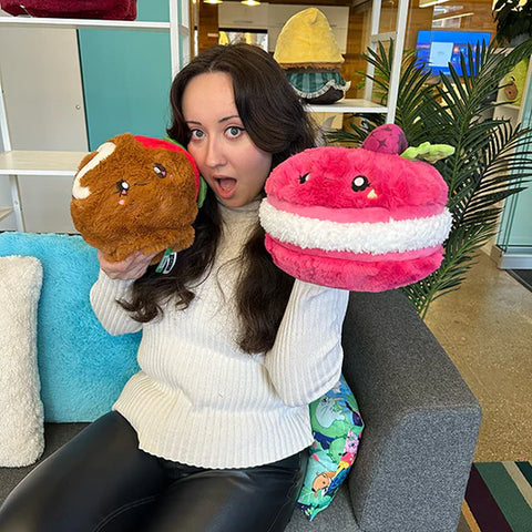 Image shows a woman holding the stuffed raspberry macaron, which is slightly larger than her head.