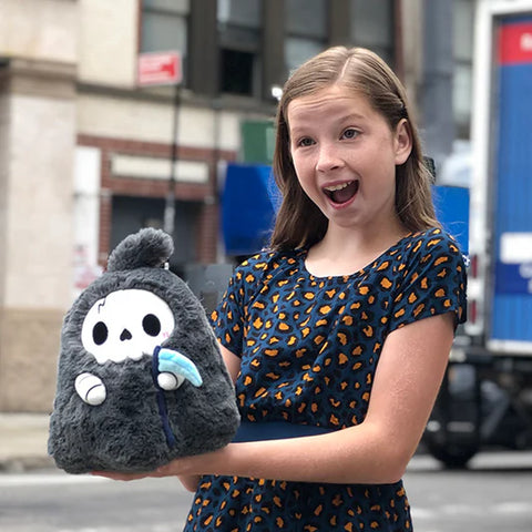 A young girl holds the plush reaper. It is slightly larger than her head.