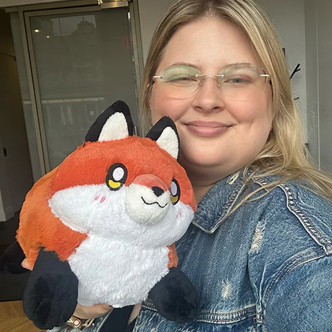 Image shows a woman holding the stuffed red fox. It is slightly larger than her head.