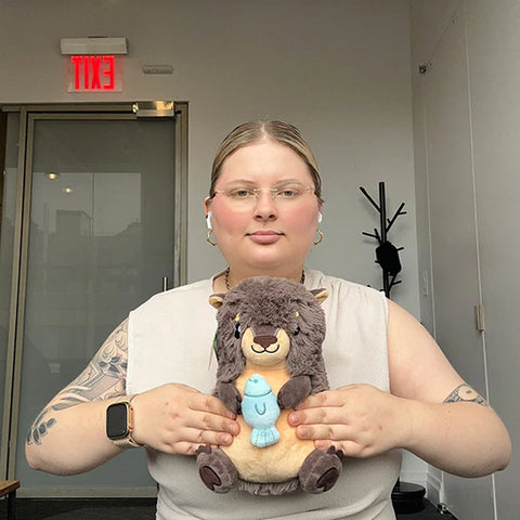 Image shows a woman holding the stuffed river otter. It is slightly larger than her head.