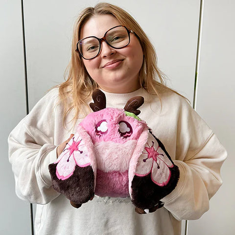 Image shows a woman holding the stuffed Sakura-themed baby mothman. It is slightly larger than her head.
