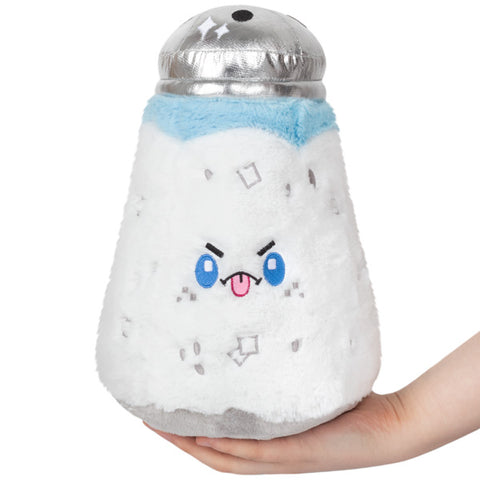 A plush toy shaped like a salt shaker with a character face on it, predominantly white with blue and other colors as accents, held in someone's hand.