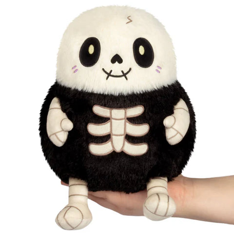 Plush toy with skeleton design held in a hand against a white background